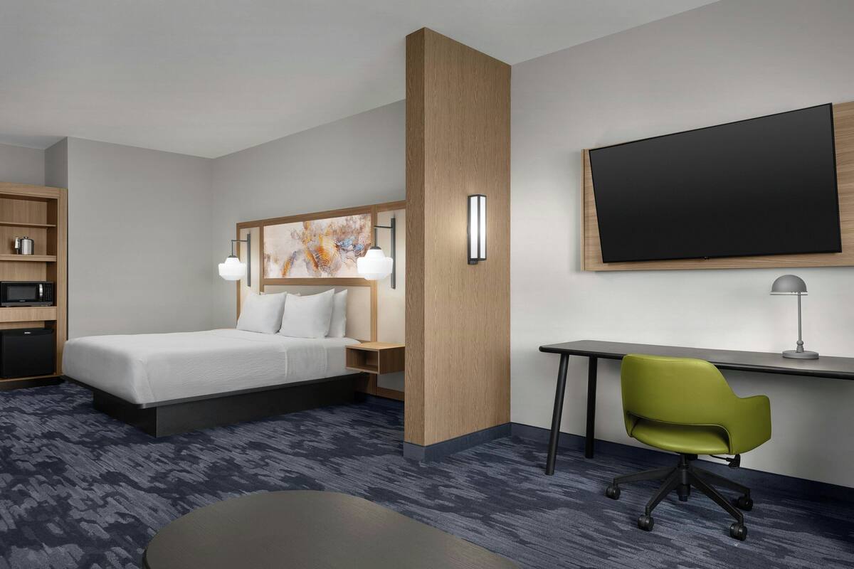 A hotel room with a bed, desk, chair, and a flat-screen TV.