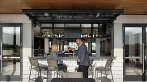 An outdoor bar area with a modern design, featuring a counter, bar stools, and a seating area with chairs.