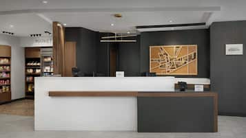 Uma área de recepção de hotel com design moderno, incluindo um balcão de atendimento, uma placa indicando um mercado e uma grande obra de arte abstrata na parede.