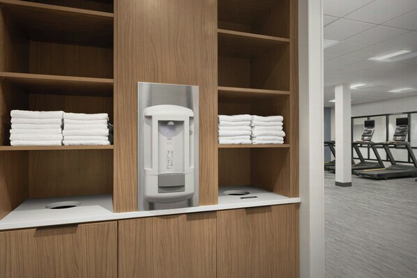 A hotel bathroom with wooden shelves holding towels, a towel dispenser, and a white countertop.