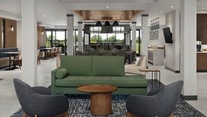 A modern lobby with a green sofa, two armchairs, a wooden coffee table, and a patterned rug.