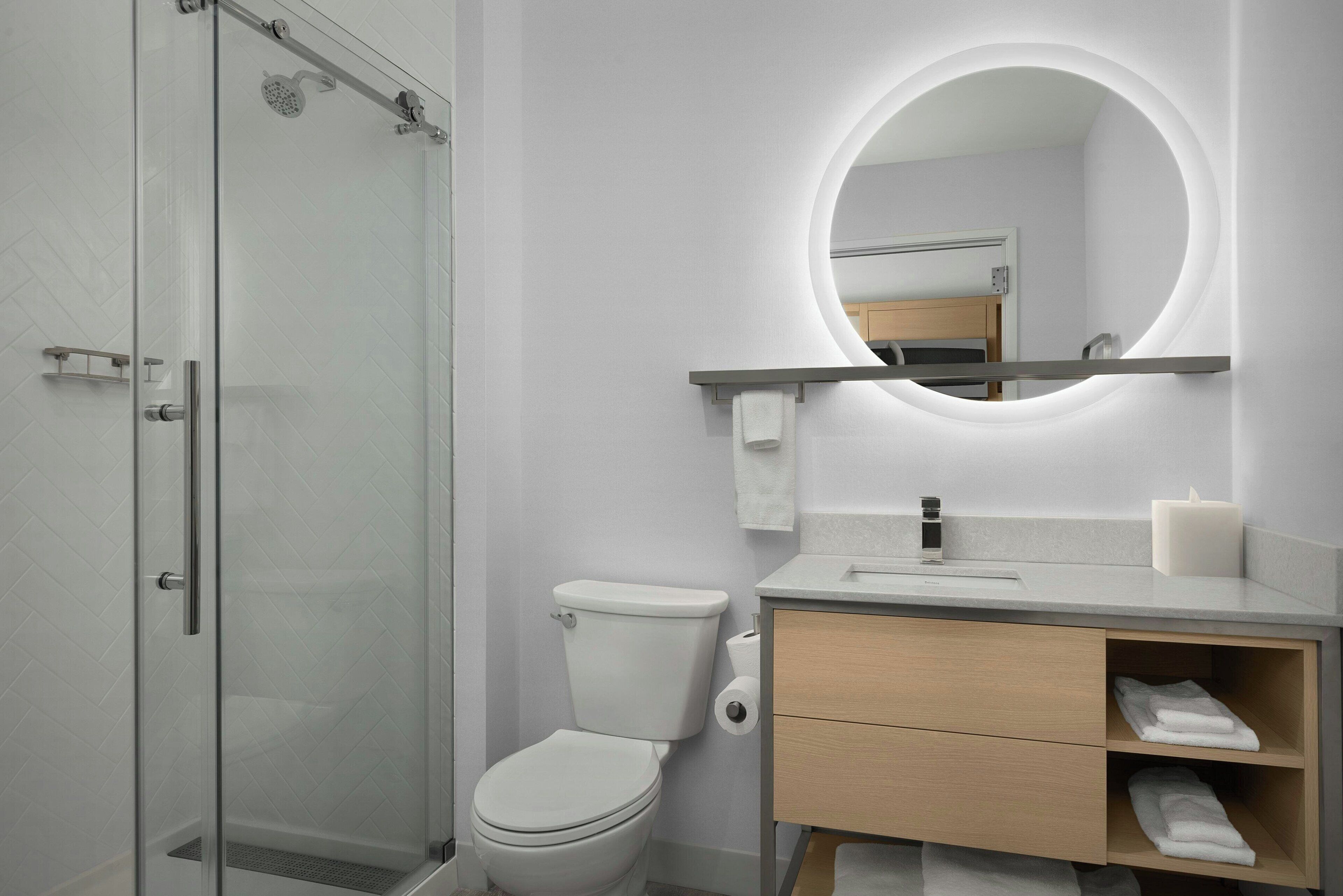 Un baño moderno con ducha envuelta en vidrio, inodoro, tocador con espejo y lavamanos.