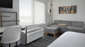 A modern hotel room with a large window, a gray sofa, a small round table, a white chair, and a bed.