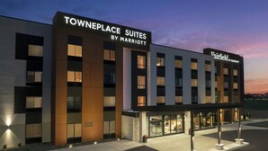 A modern hotel with a sign reading "Towneplace Suites by Marriott Fairfield." It features a flat roof, large windows, and a well-lit entrance.