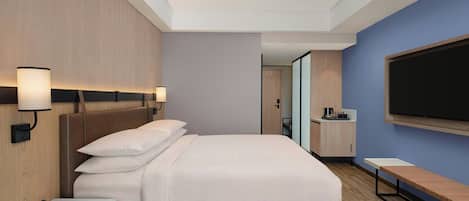 A modern hotel room with a large bed, bedside lamps, a TV, a small desk, and a bench.
