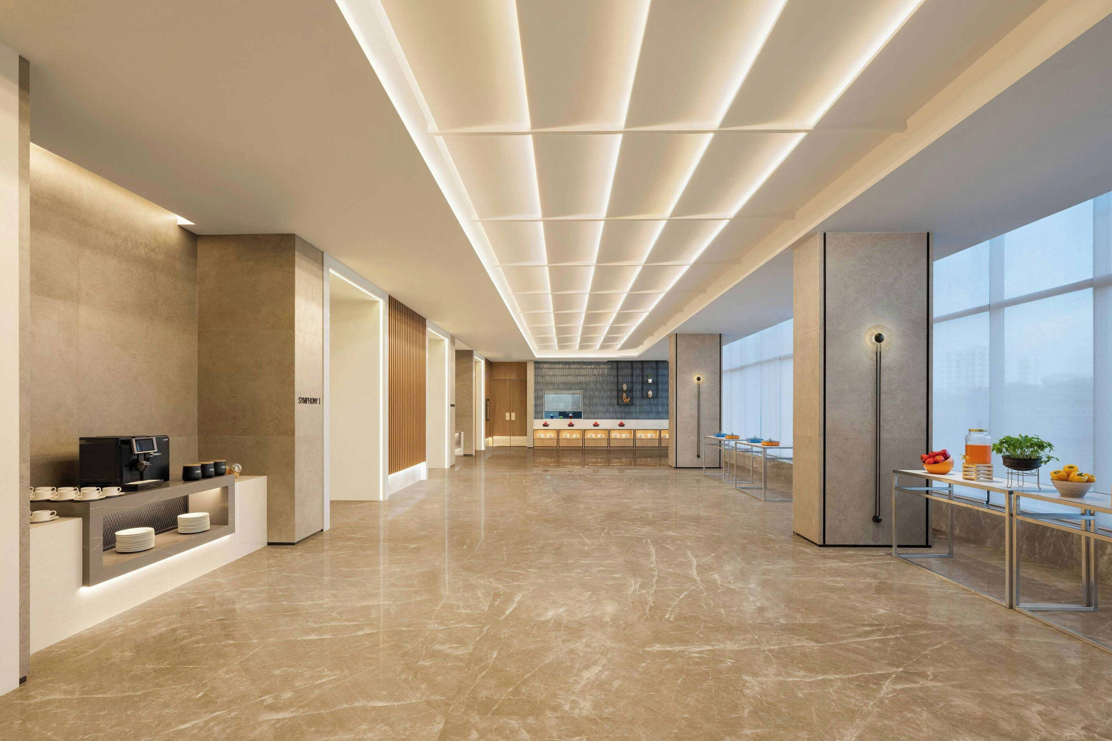 A spacious, modern lobby with a long corridor, a reception desk, and a seating area with a view of the city.