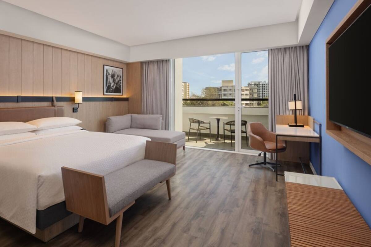 A hotel room with a large bed, a desk, a chair, and a balcony with a view.