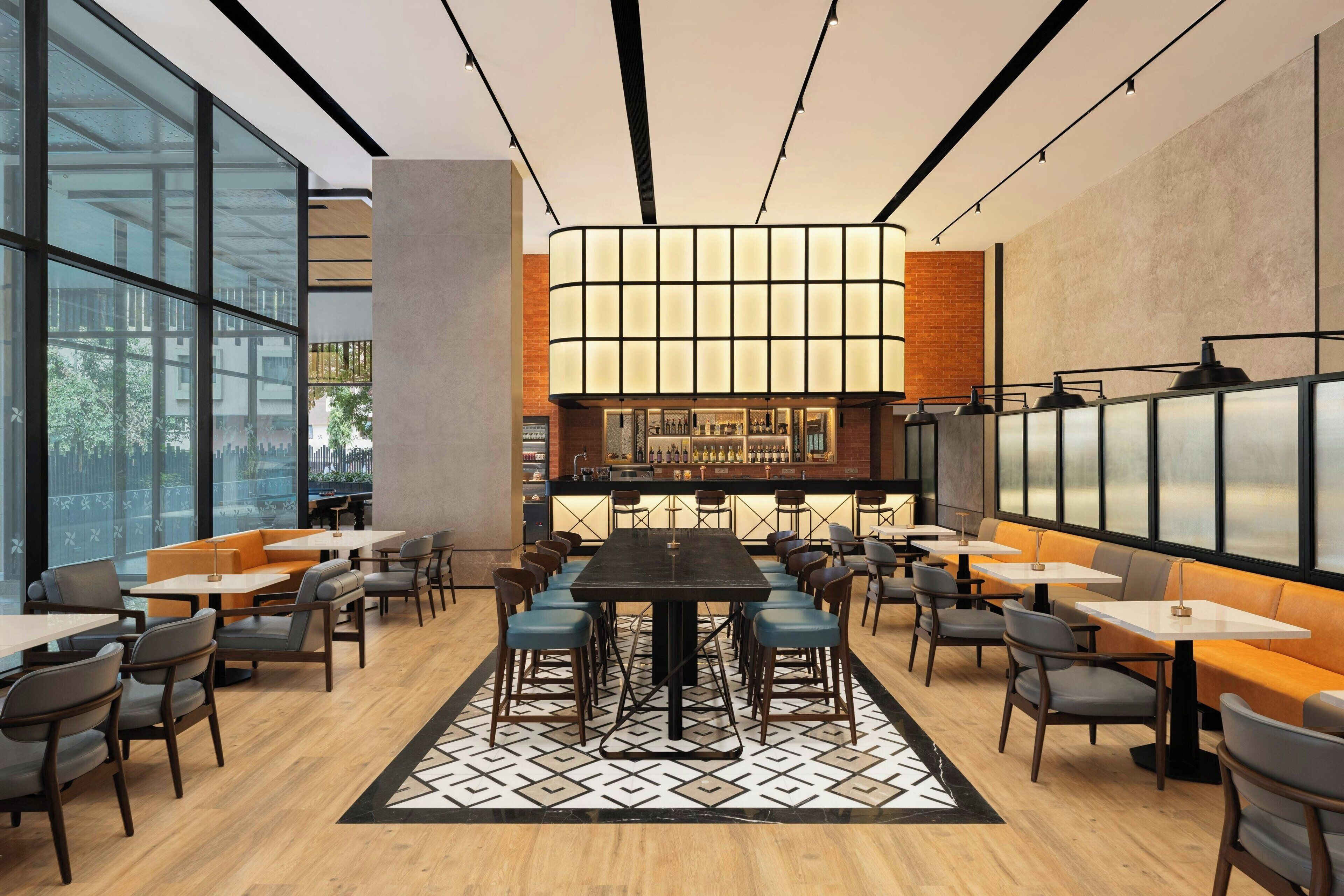 A modern restaurant with a central bar, high ceilings, and large windows.