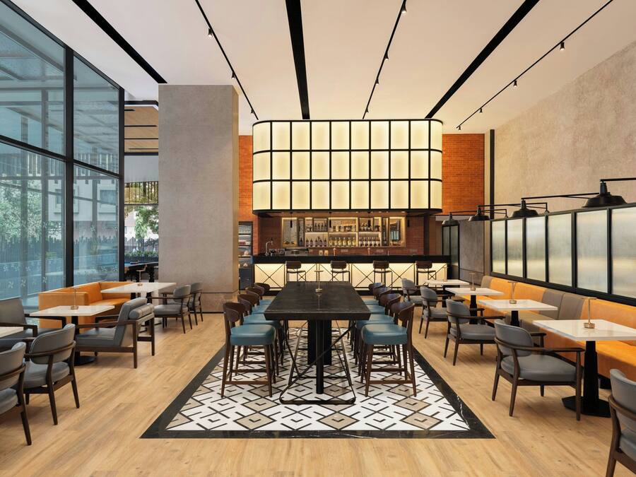 A modern restaurant with a central bar, high ceilings, and large windows.