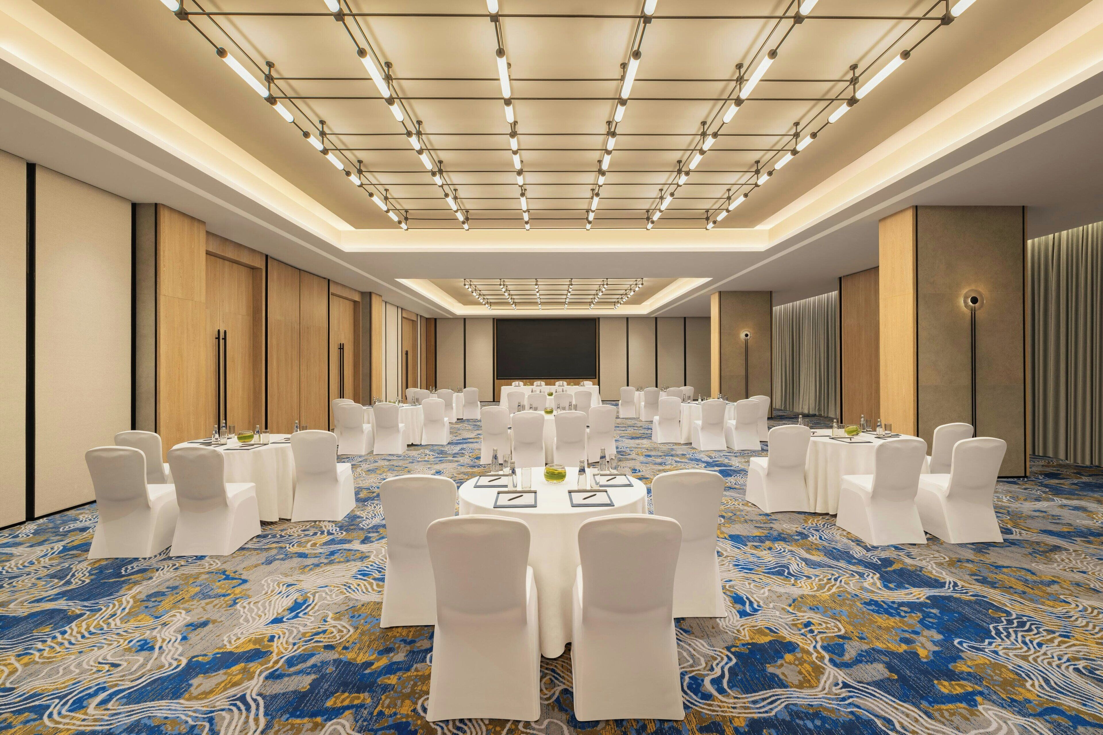A conference room with round tables, white chairs, and a patterned carpet.