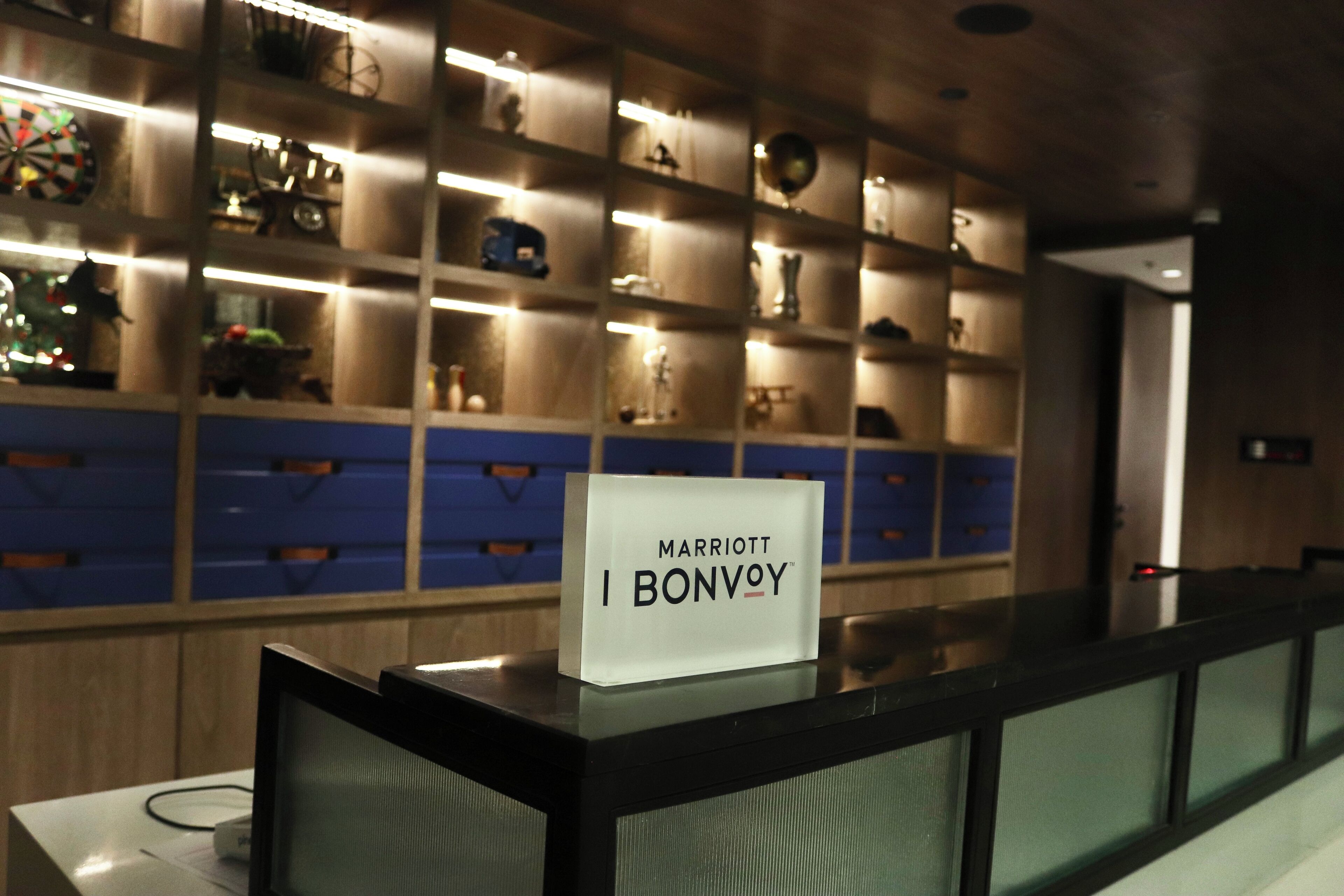 A reception desk with a sign reading "Marriott Bonvoy" in a hotel lobby with shelves displaying various items.