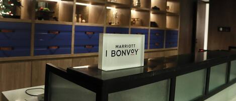 A reception desk with a sign reading "Marriott Bonvoy" in a hotel lobby with shelves displaying various items.