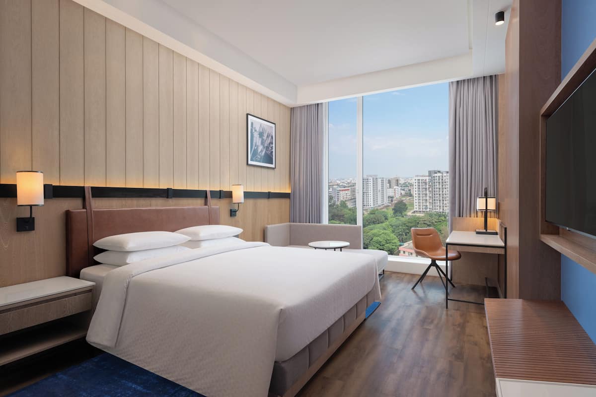 A modern hotel room with a large bed, a desk, a chair, and a TV.