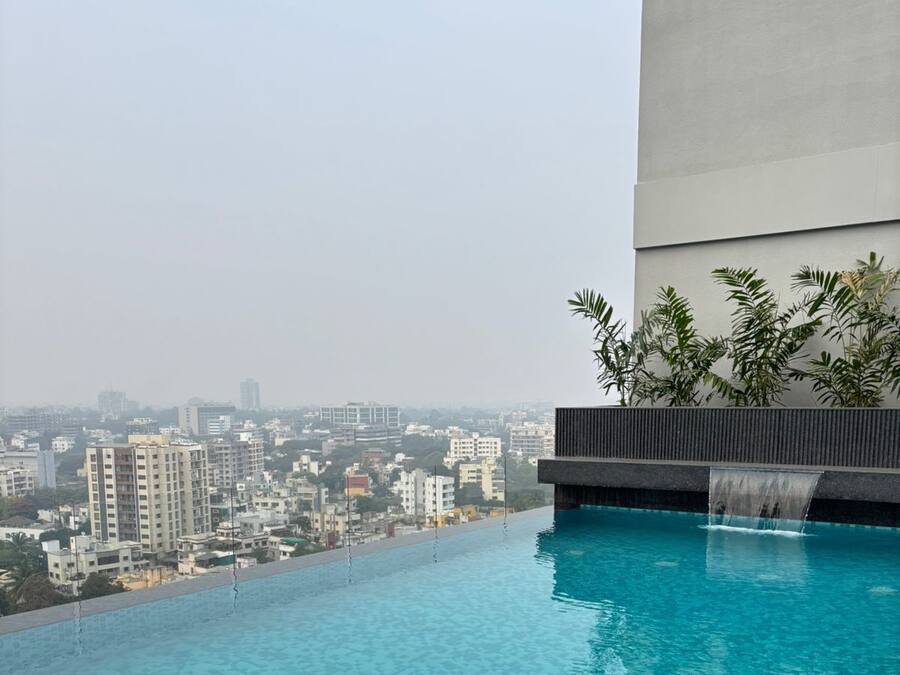 A rooftop infinity pool with a city view, surrounded by a modern building and some greenery.