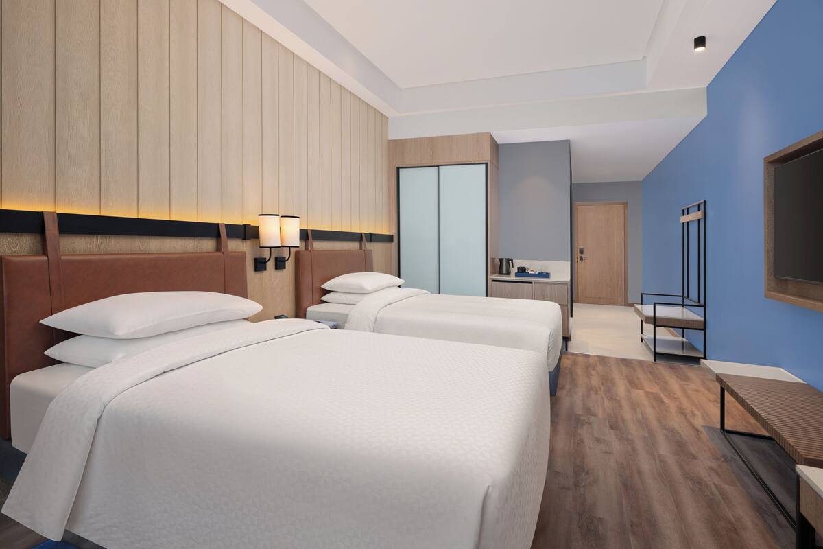 A hotel room with two beds, a desk, a chair, a TV, and a wardrobe.