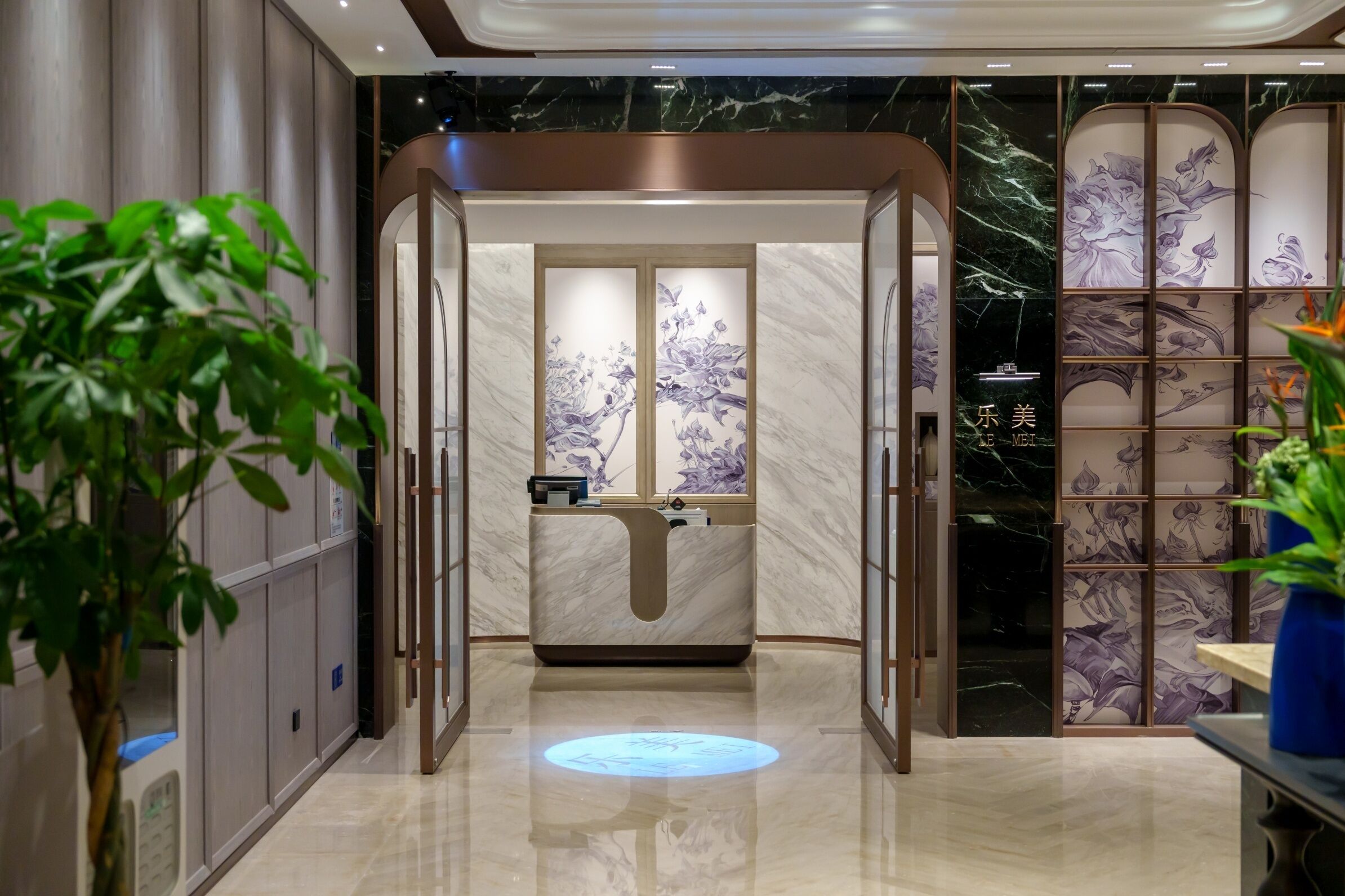 A modern hotel lobby with a reception desk, a digital information display, and a decorative wall with floral patterns.