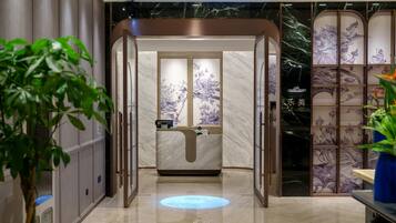 A modern hotel lobby with a reception desk, a digital information display, and a decorative wall with floral patterns.