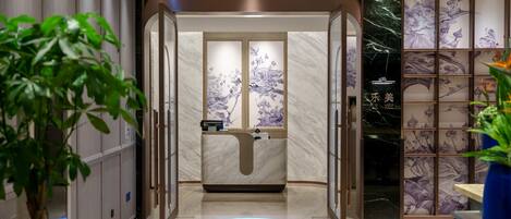 A modern hotel lobby with a reception desk, a digital information display, and a decorative wall with floral patterns.