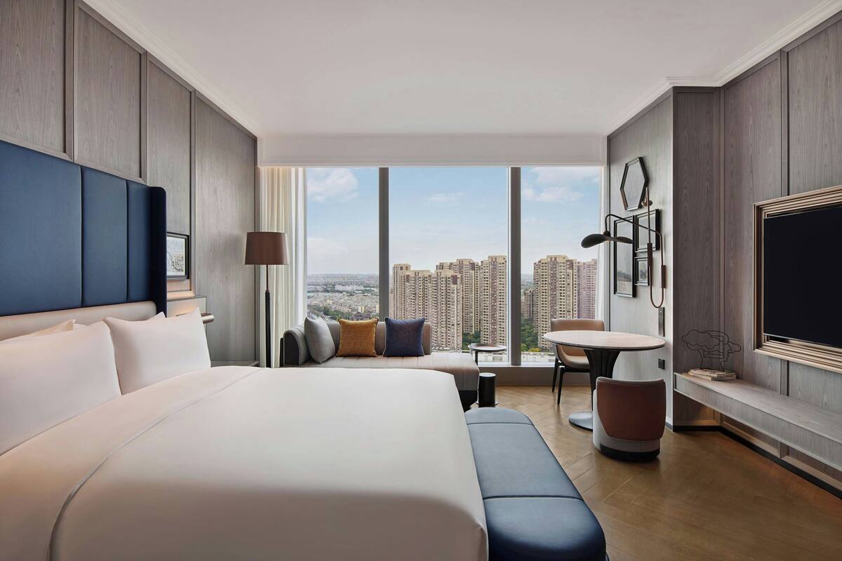 Une chambre d’hôtel moderne dotée d’un grand lit, d’un coin salon, d’une table à manger et offrant une vue sur la ville.