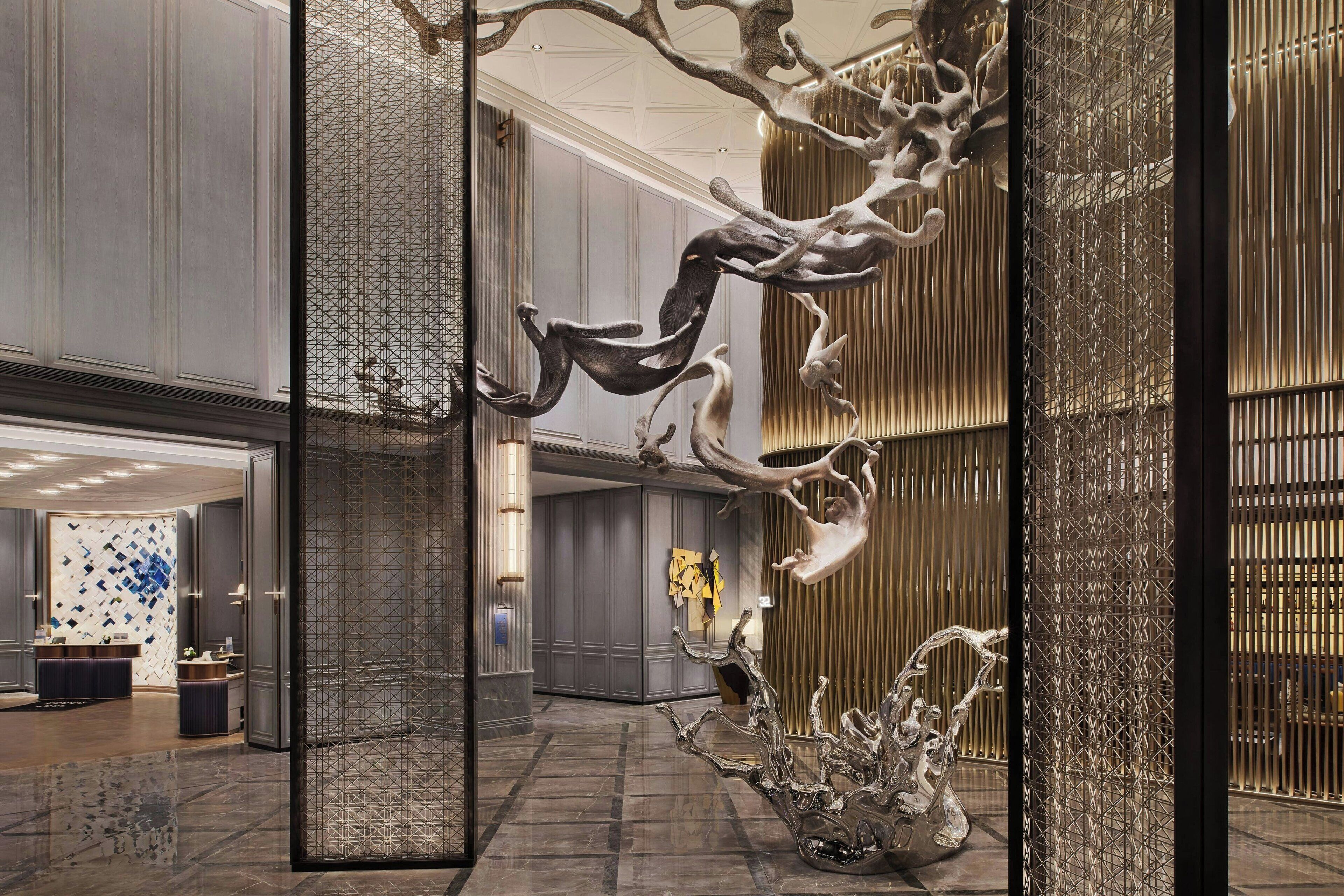 A modern lobby with a large glass partition, a reception desk, and a decorative metal sculpture.