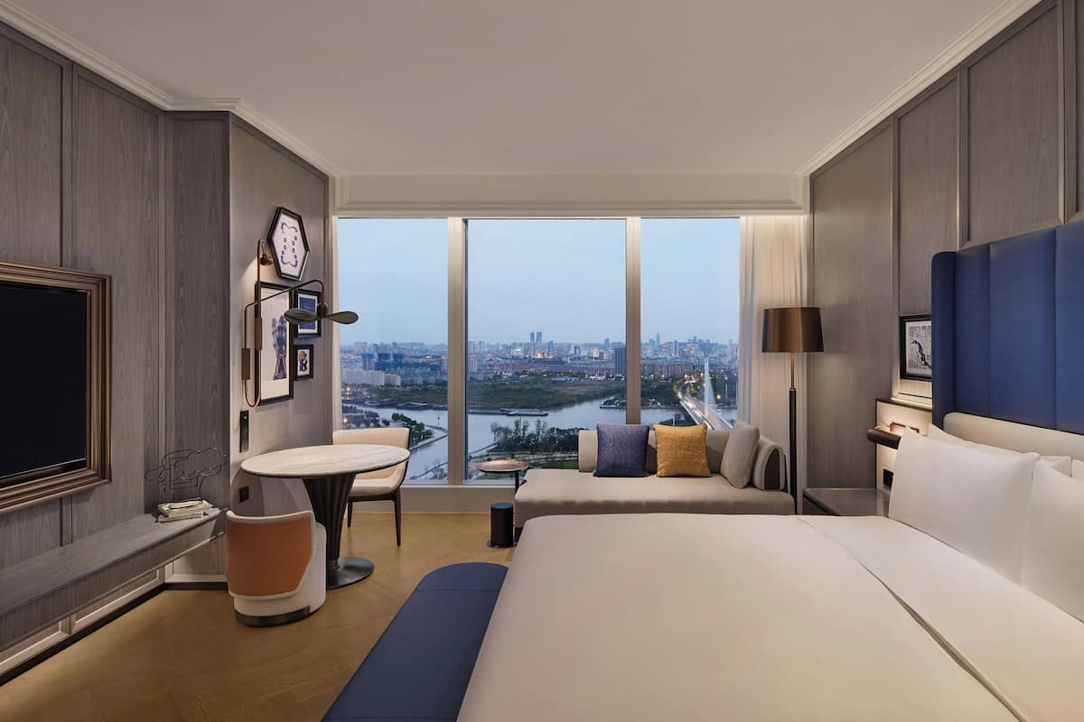 Une chambre d’hôtel moderne dotée d’un grand lit, d’un coin salon, d’une télévision et offrant une vue sur la ville.