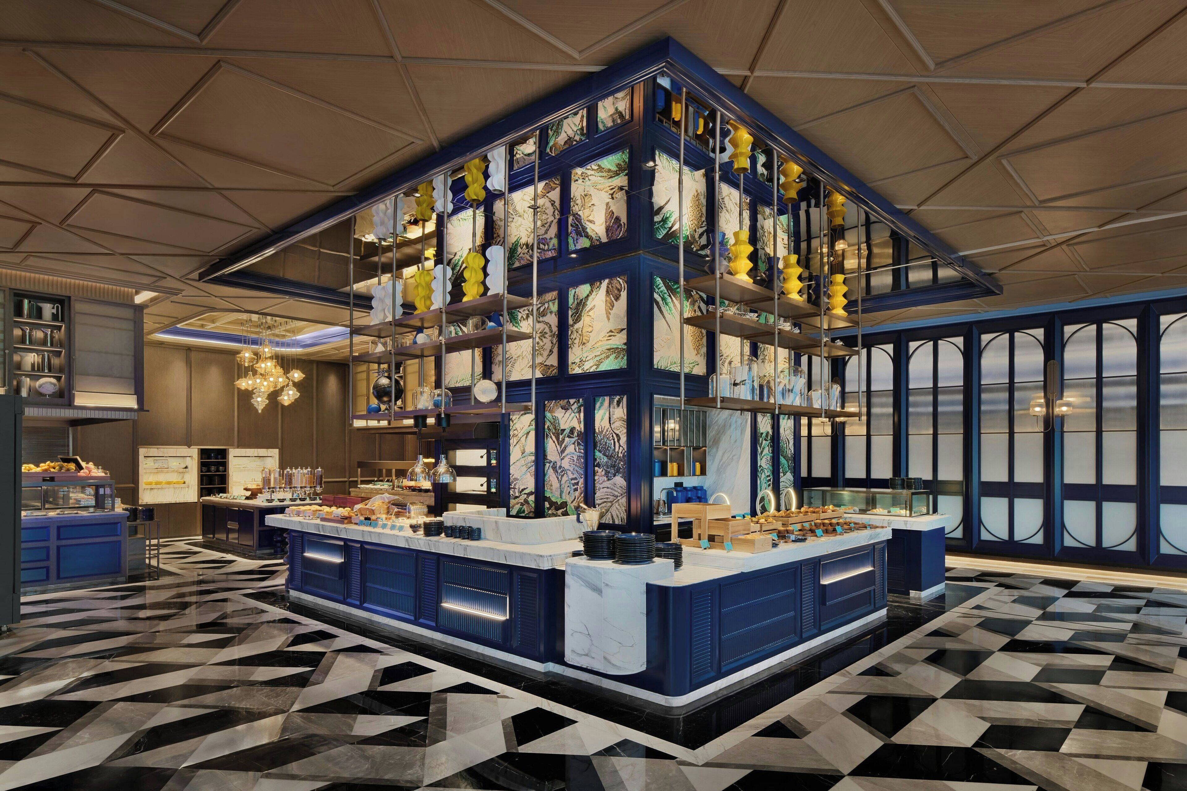 A modern hotel lobby with a central bar area, large windows, and a geometric patterned floor.