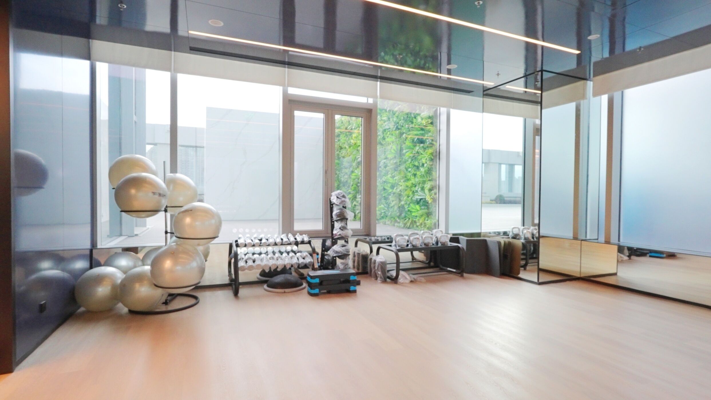A modern gym with exercise equipment, large windows, and a view of greenery outside.
