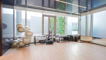 A modern gym with exercise equipment, large windows, and a view of greenery outside.