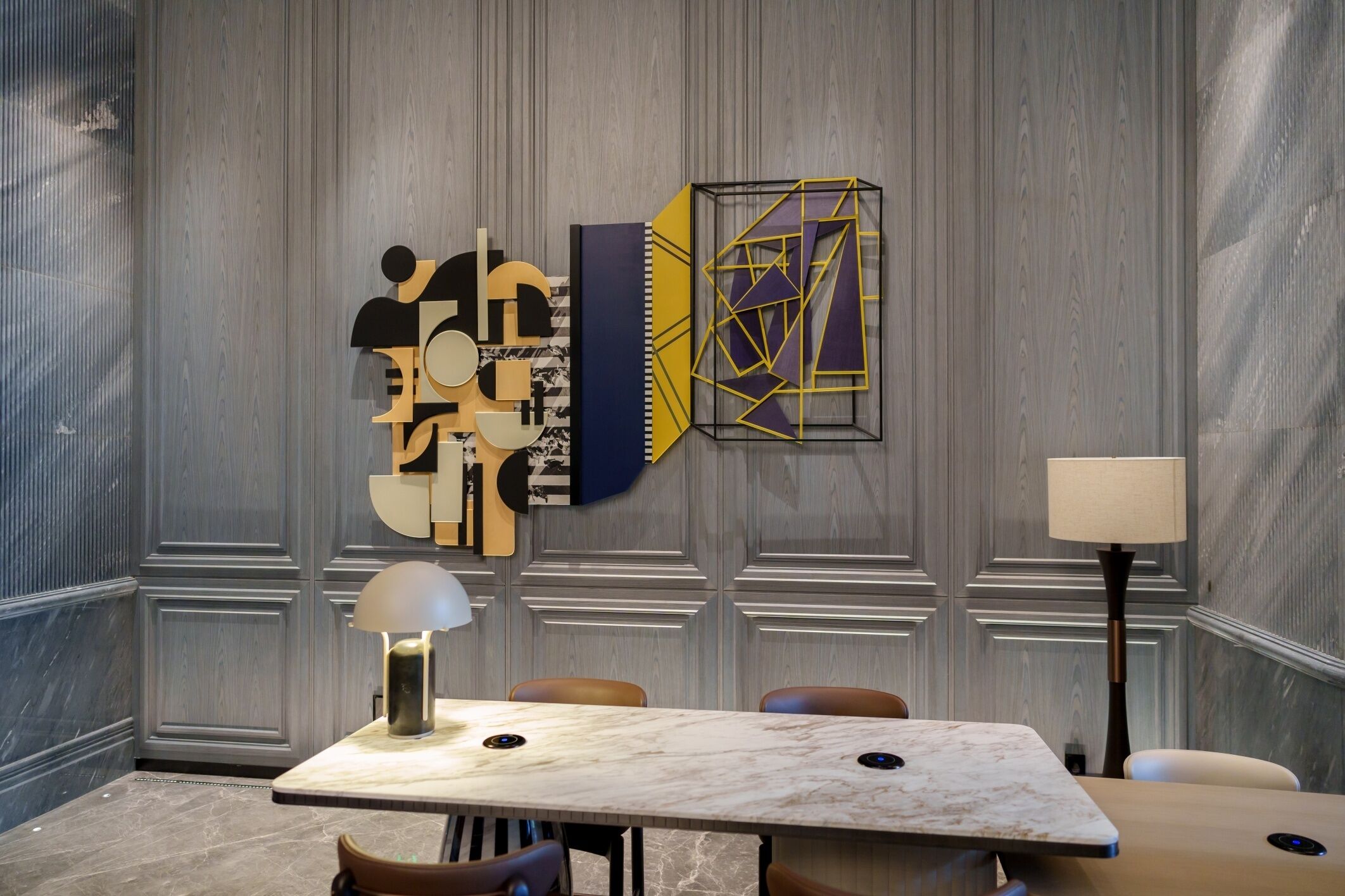 Un salón de conferencias con una mesa de mármol, sillas de cuero, una lámpara de pie y arte abstracto en la pared.