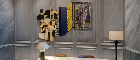 Un salón de conferencias con una mesa de mármol, sillas de cuero, una lámpara de pie y arte abstracto en la pared.
