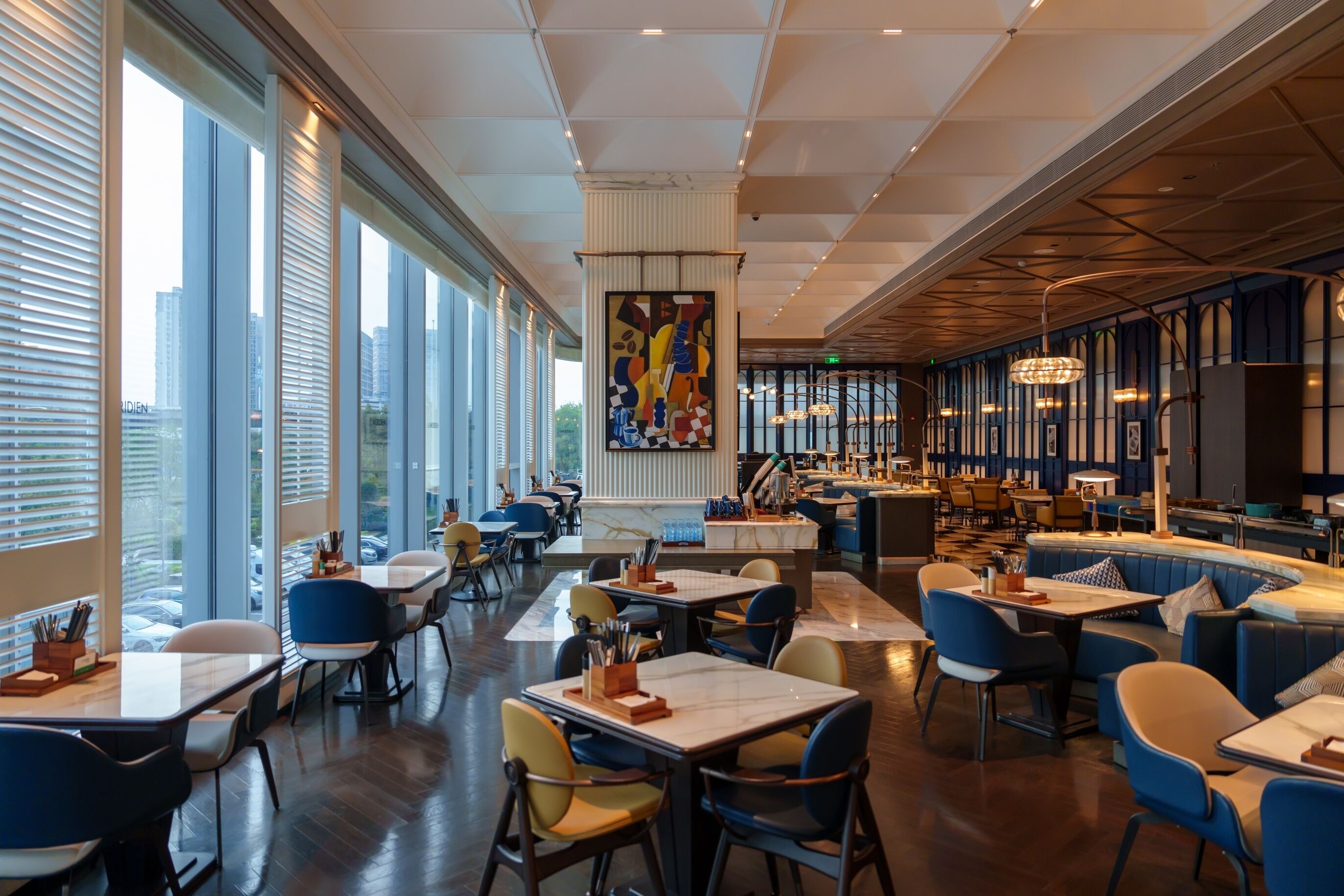 Un restaurant moderne doté de hauts plafonds, de grandes fenêtres et offrant différents types de sièges, notamment des tables et des banquettes.