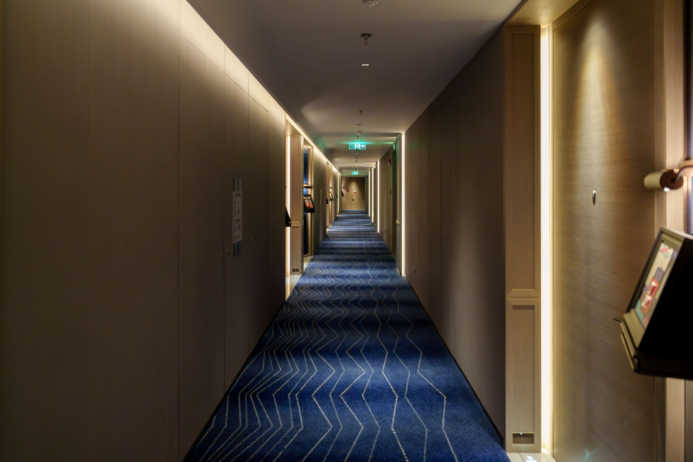 A hotel hallway with a blue carpet, wooden walls, and a framed picture on the right.