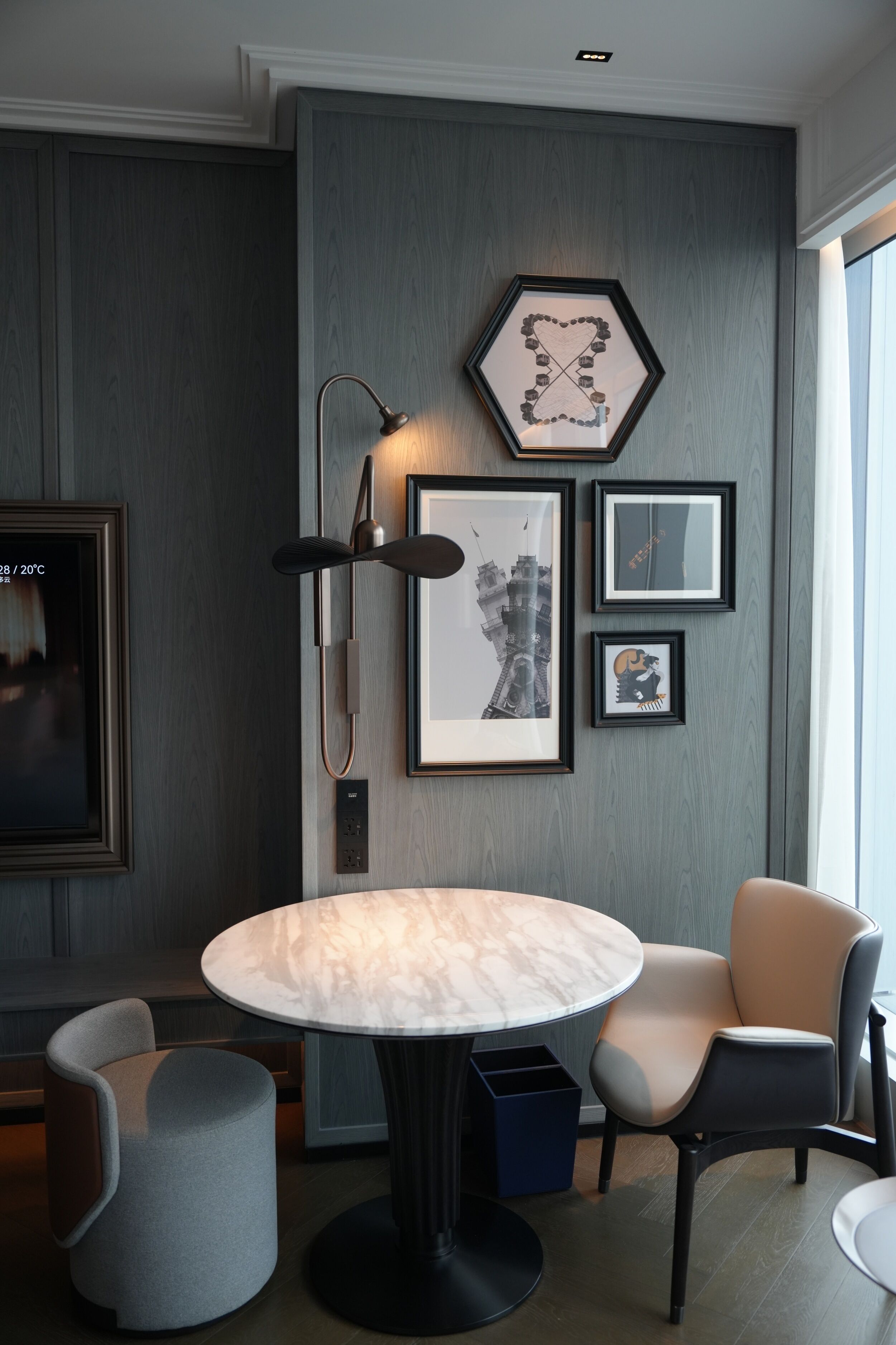 A modern room with a round marble table, two chairs, a floor lamp, and framed artwork on the wall.
