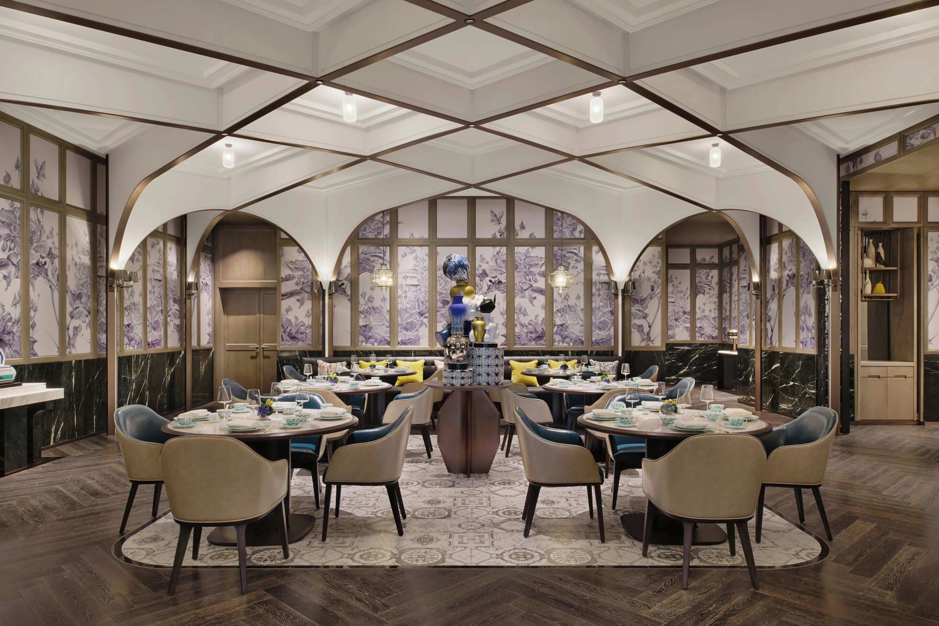 A spacious dining area with high ceilings and arched windows, featuring a central round table surrounded by chairs.