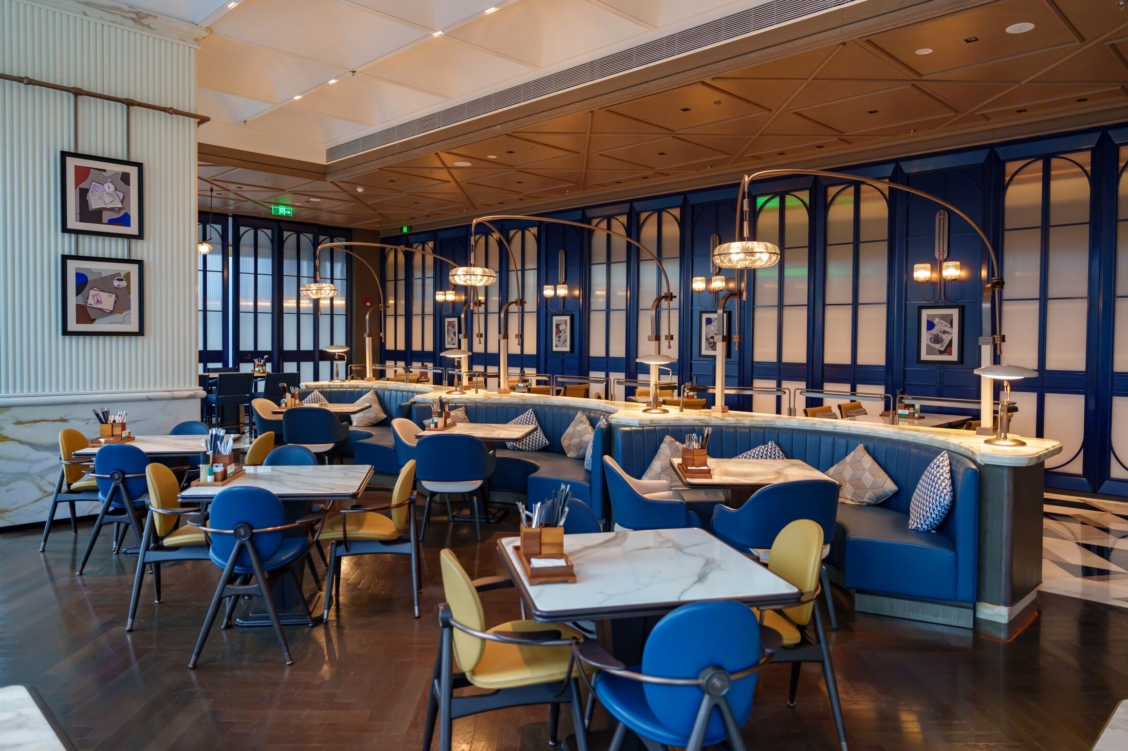 Un restaurante con asientos tipo banca azules, mesas redondas y una zona de bar.