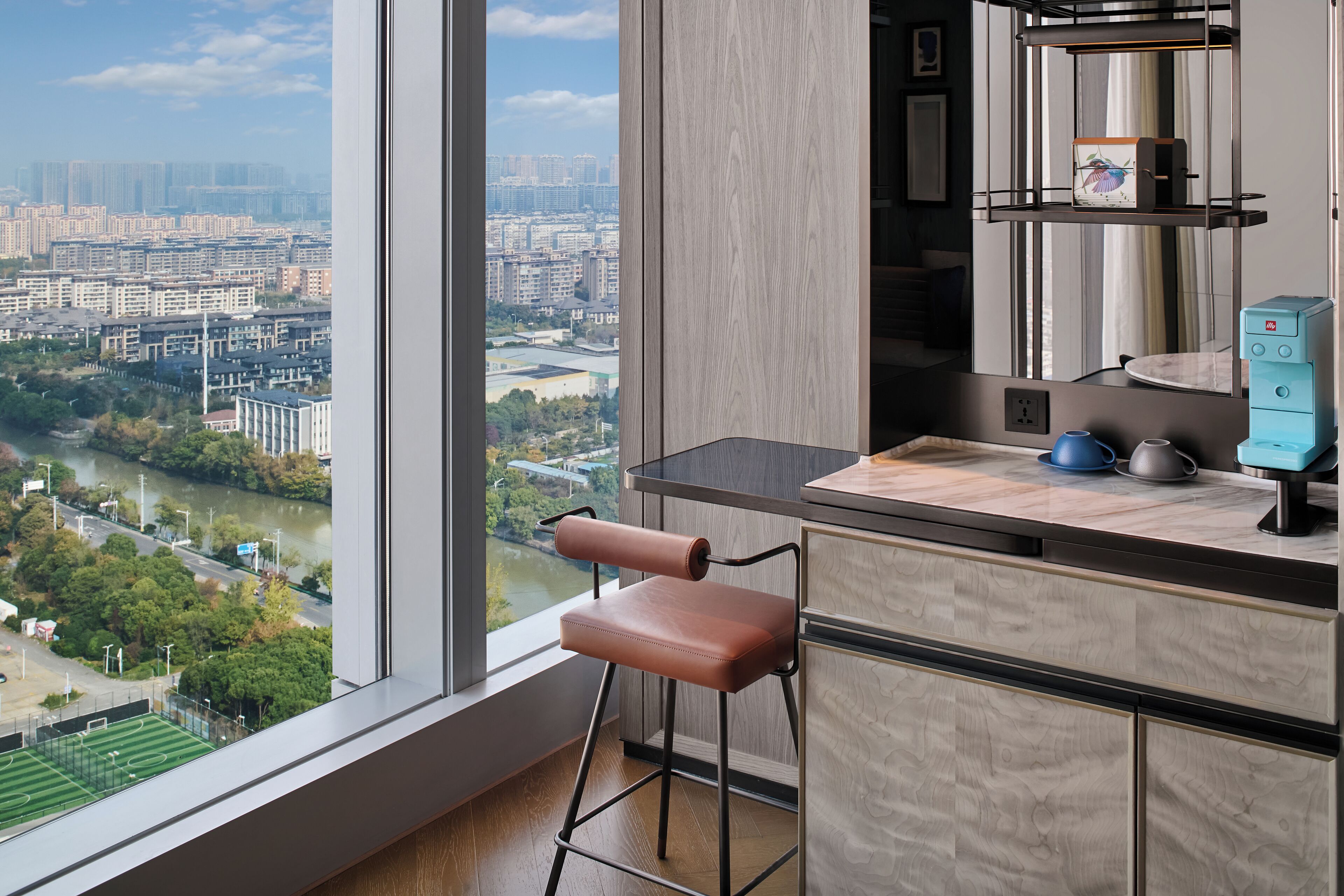 A modern kitchen with a view of a cityscape, a bar stool, and a countertop with kitchen appliances.