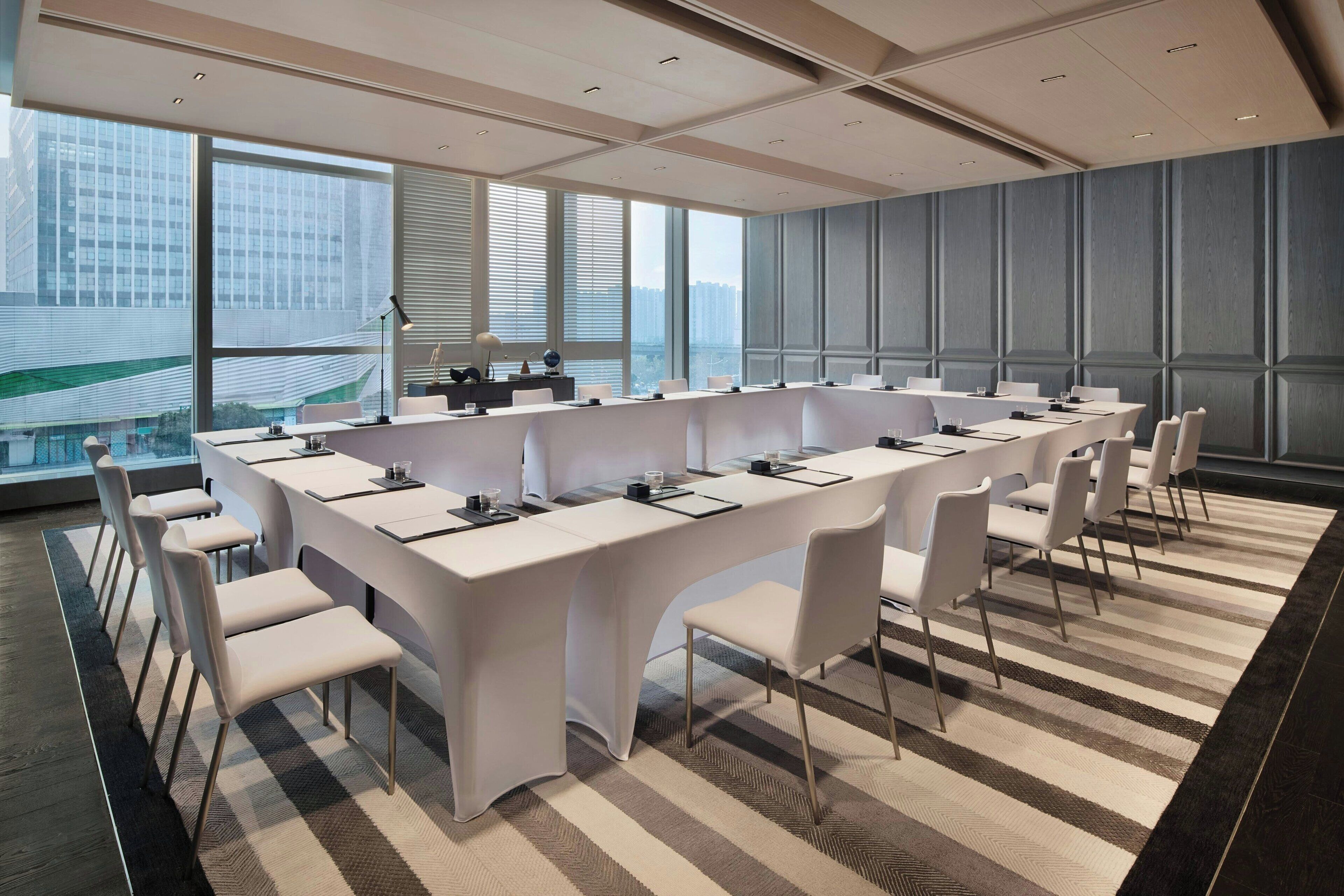 Une salle de conférence avec une longue table, des chaises blanches et un tapis à carreaux.