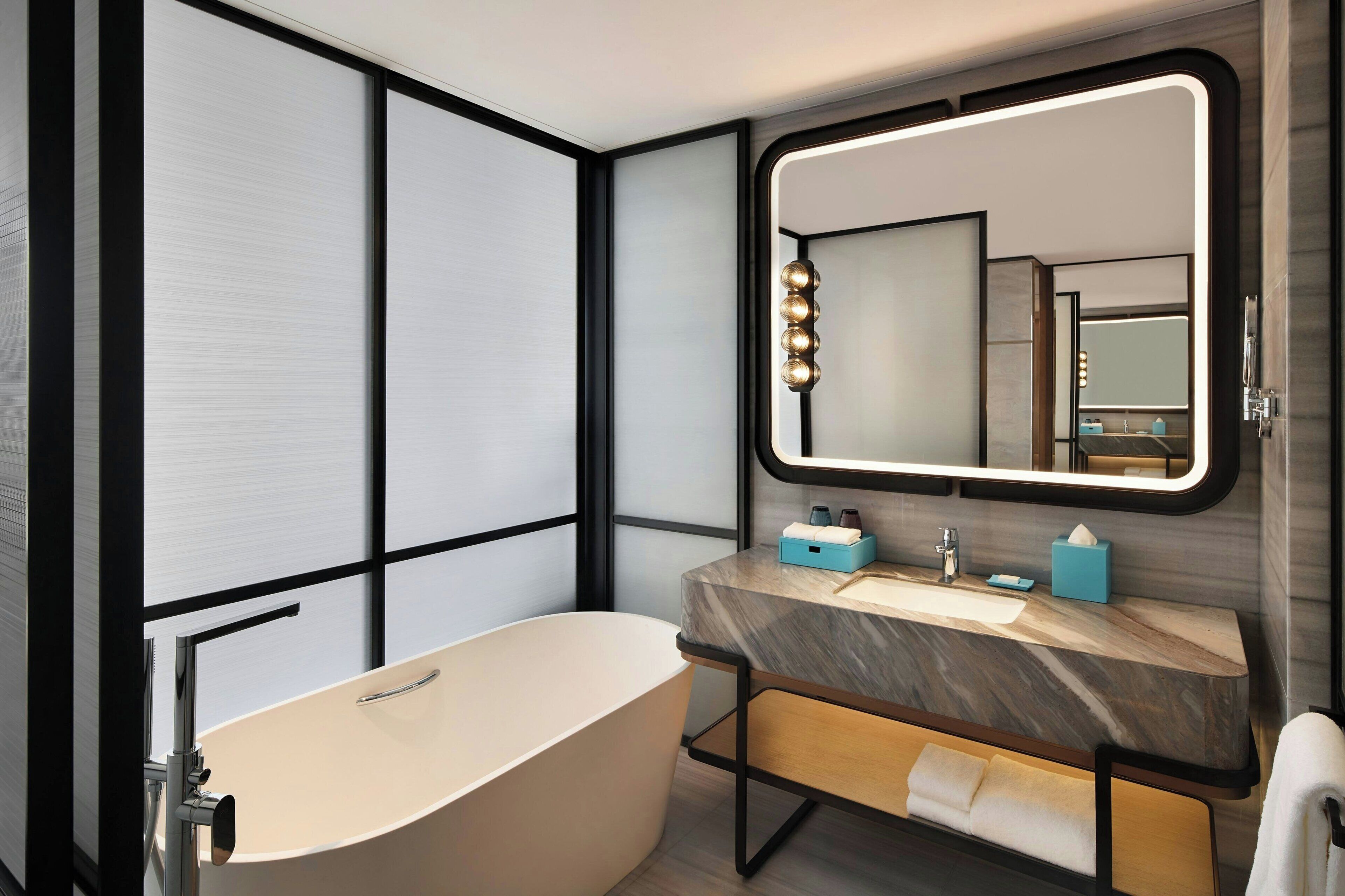Ein modernes Badezimmer mit einer freistehenden Badewanne, einem Waschtisch mit Marmorplatte und einem großen, beleuchteten Spiegel.