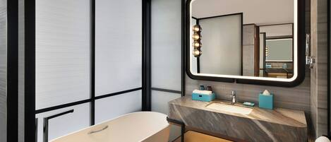 Un baño moderno con una bañera independiente, un tocador con encimera de mármol y un espejo grande con iluminación.