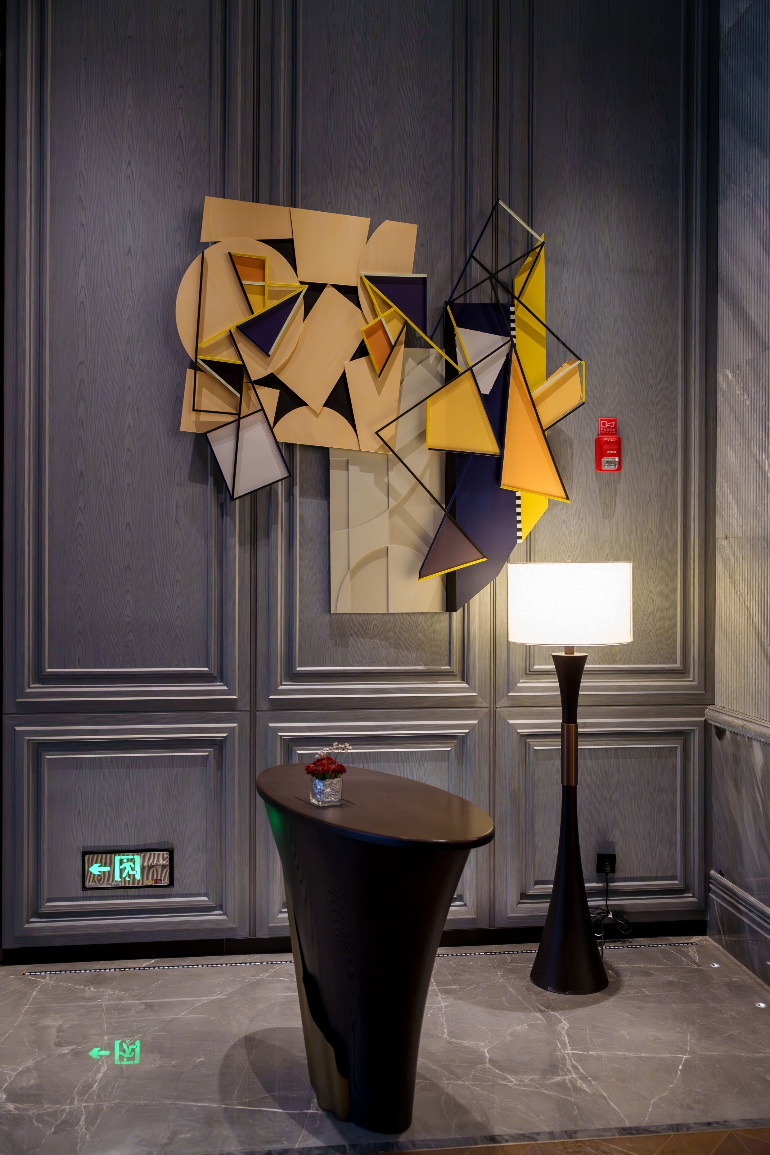 A modern interior with a geometric art piece on the wall, a table with a vase, and a floor lamp.