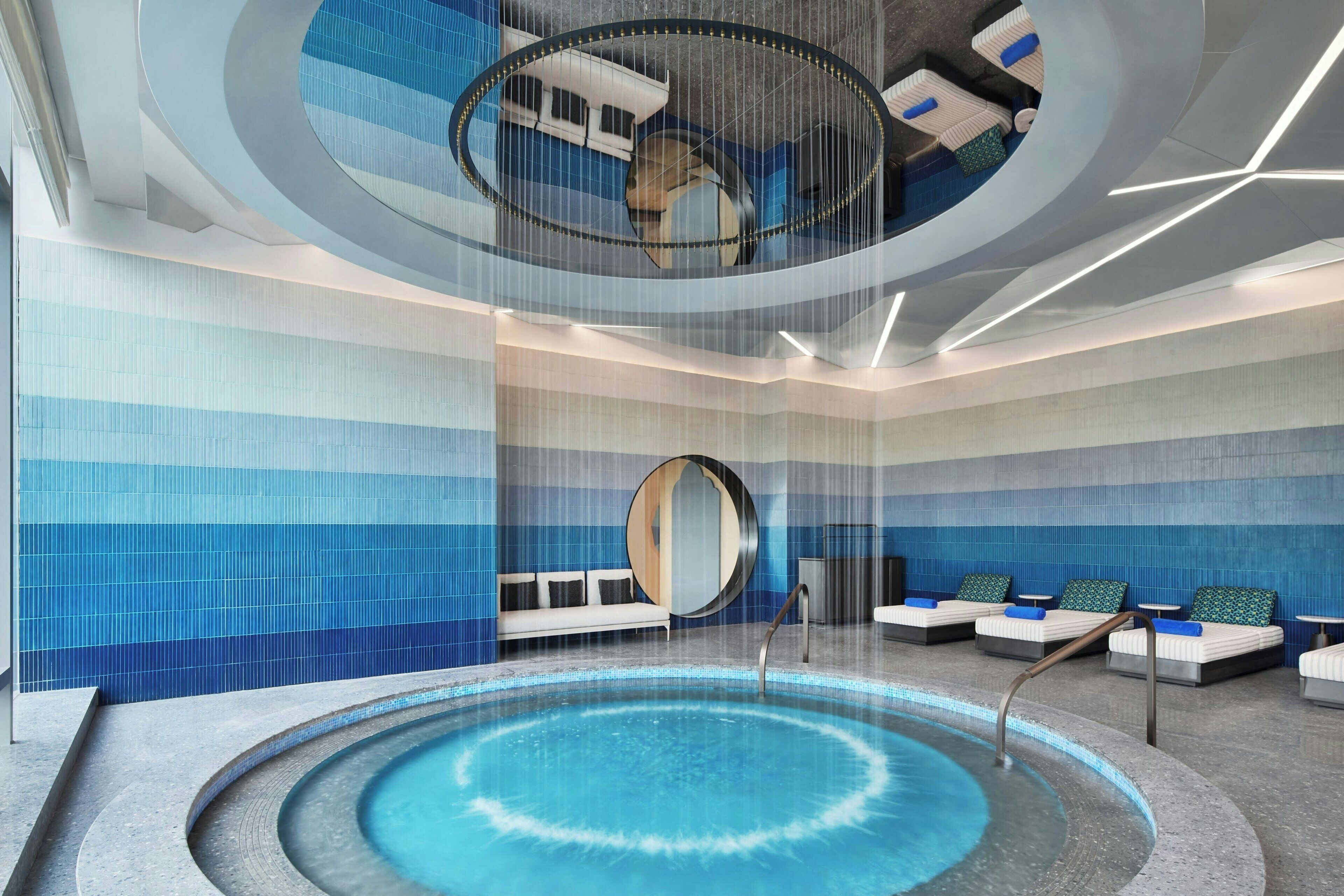 Un área de piscina interior moderna con un jacuzzi circular, asientos tipo sala y un diseño de techo original.