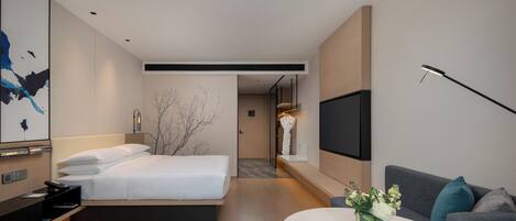 A modern hotel room with a bed, a sofa, a TV, and a small table with flowers.