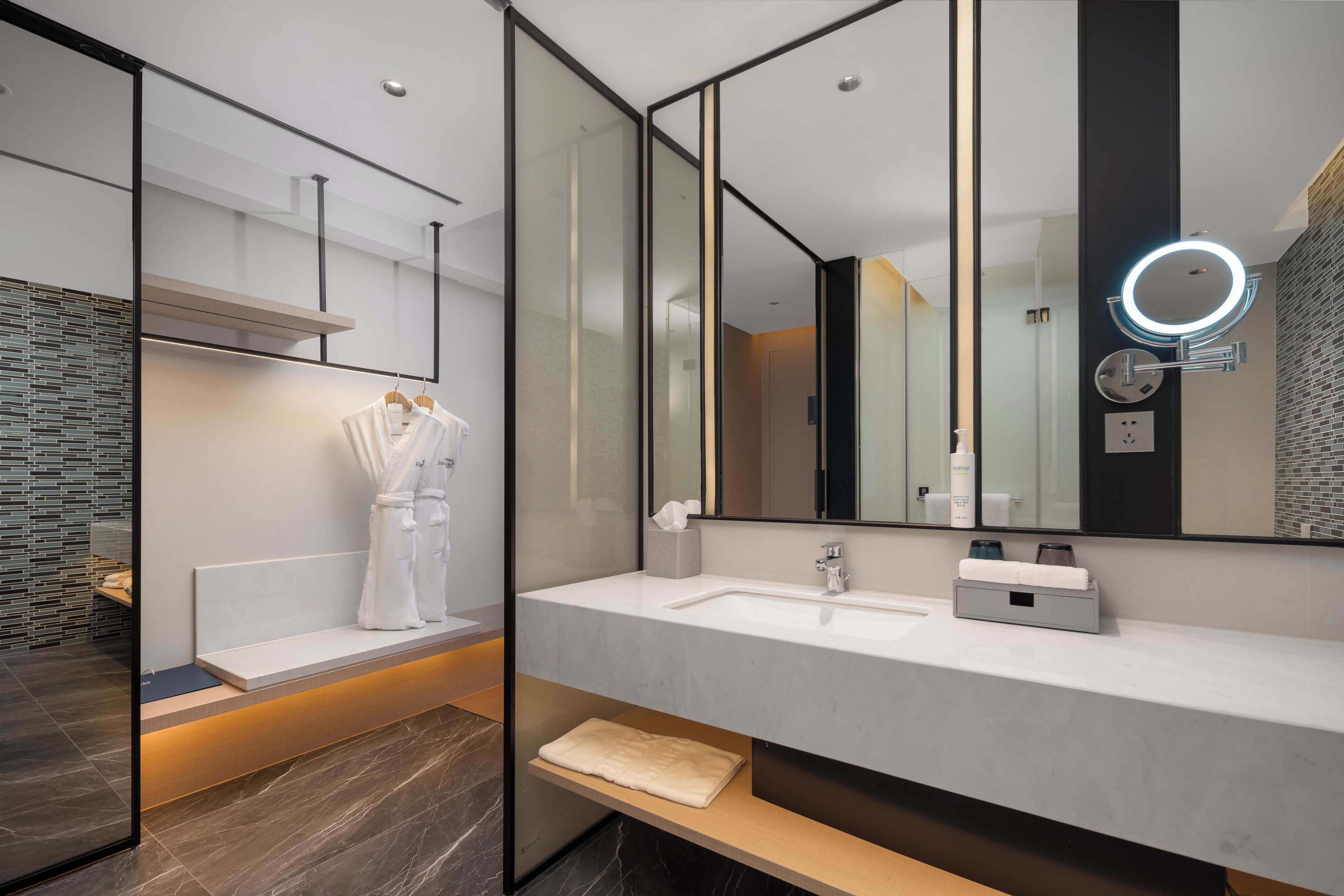 A modern bathroom with a large mirror, a white sink, and a bench.