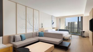 Una habitación de hotel moderna con una cama grande, un sofá, una mesa de centro y vistas a edificios altos.
