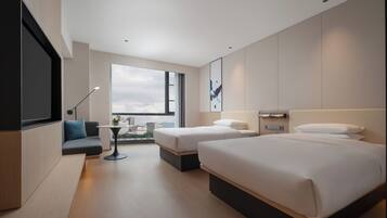 Quarto de hotel moderno com duas camas, um sofá, uma mesa pequena e uma grande janela com vista para a cidade.