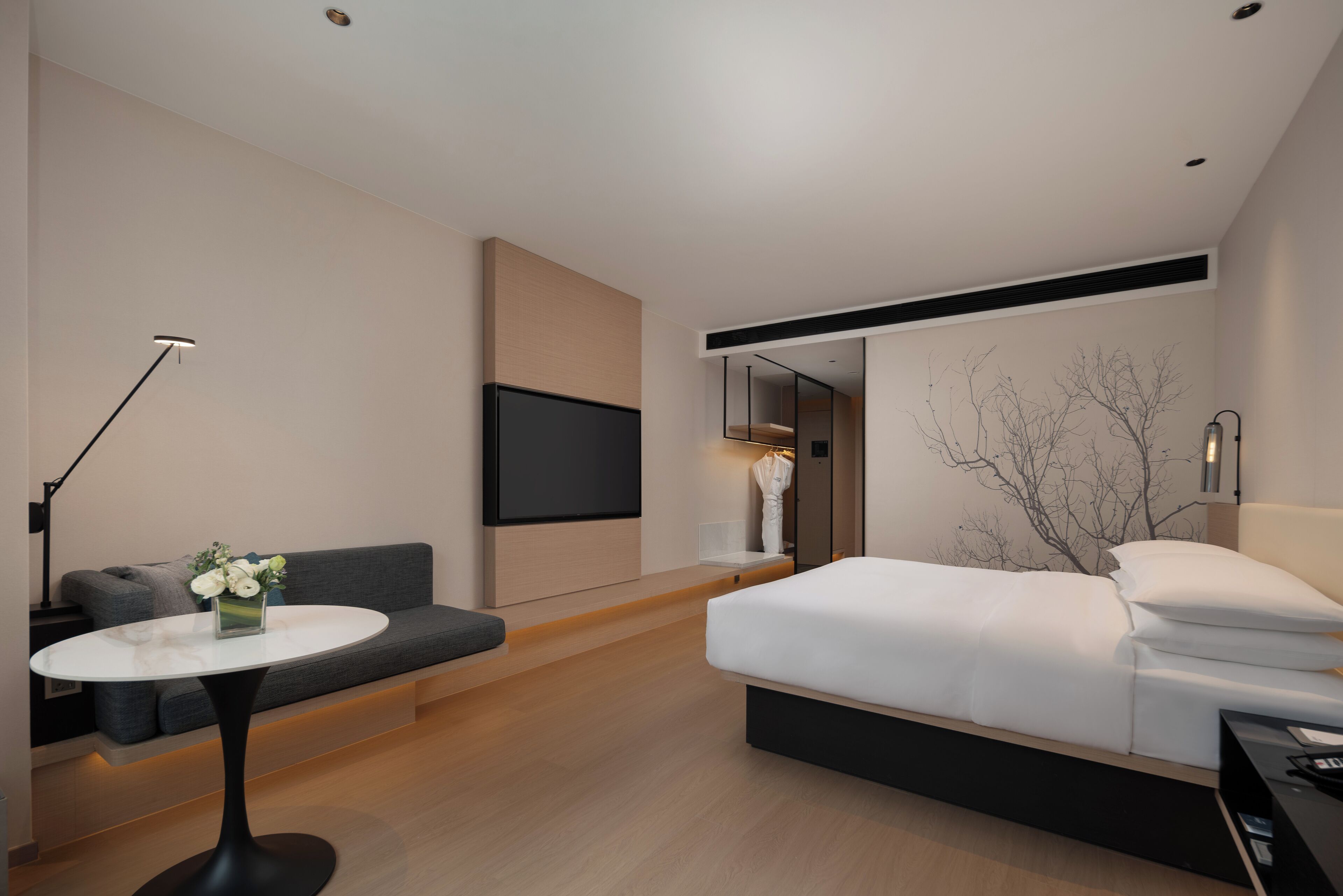 Una habitación de hotel moderna con una cama, un sofá, una mesita y un televisor montado en la pared.
