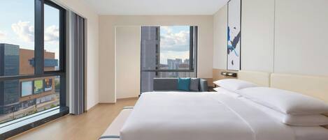 A modern hotel room with a large bed, a view of the city through floor-to-ceiling windows, and a minimalist design.