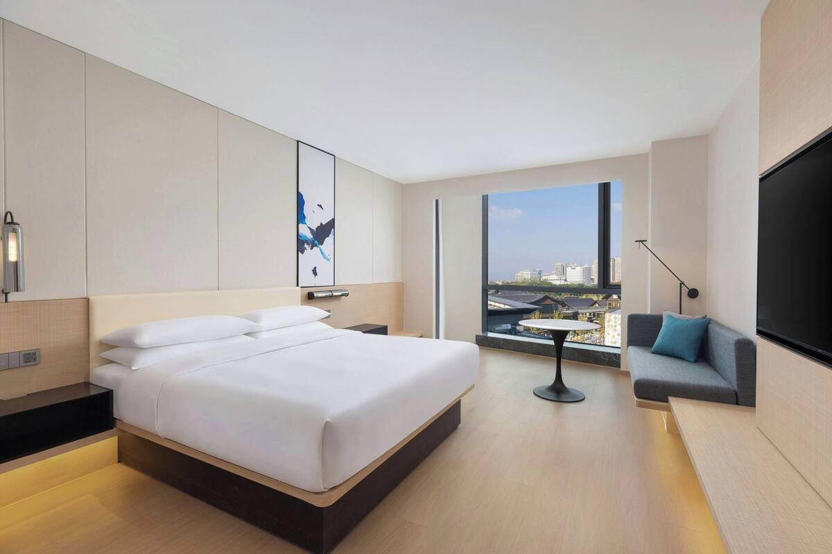 A modern hotel room with a large bed, a sofa, a small table, and a TV.