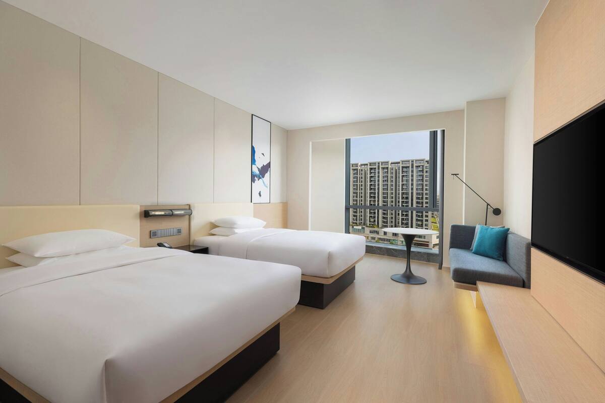 A hotel room with two beds, a sofa, a TV, a desk, and a window with a city view.