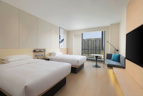 Habitación de hotel con dos camas, un sofá, un televisor, un escritorio y una ventana con vista a la ciudad.